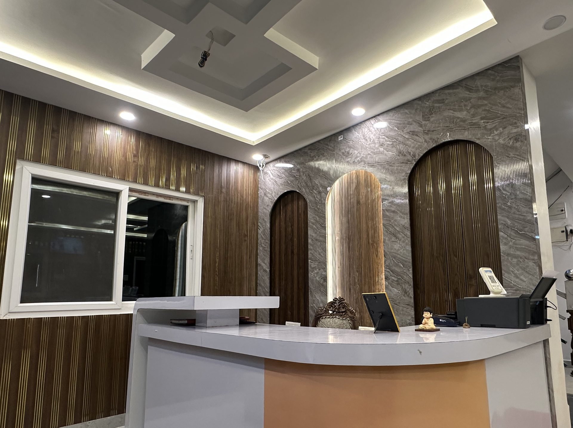 Hotel reception desk in front of a grey stone wall with arched walnut panels