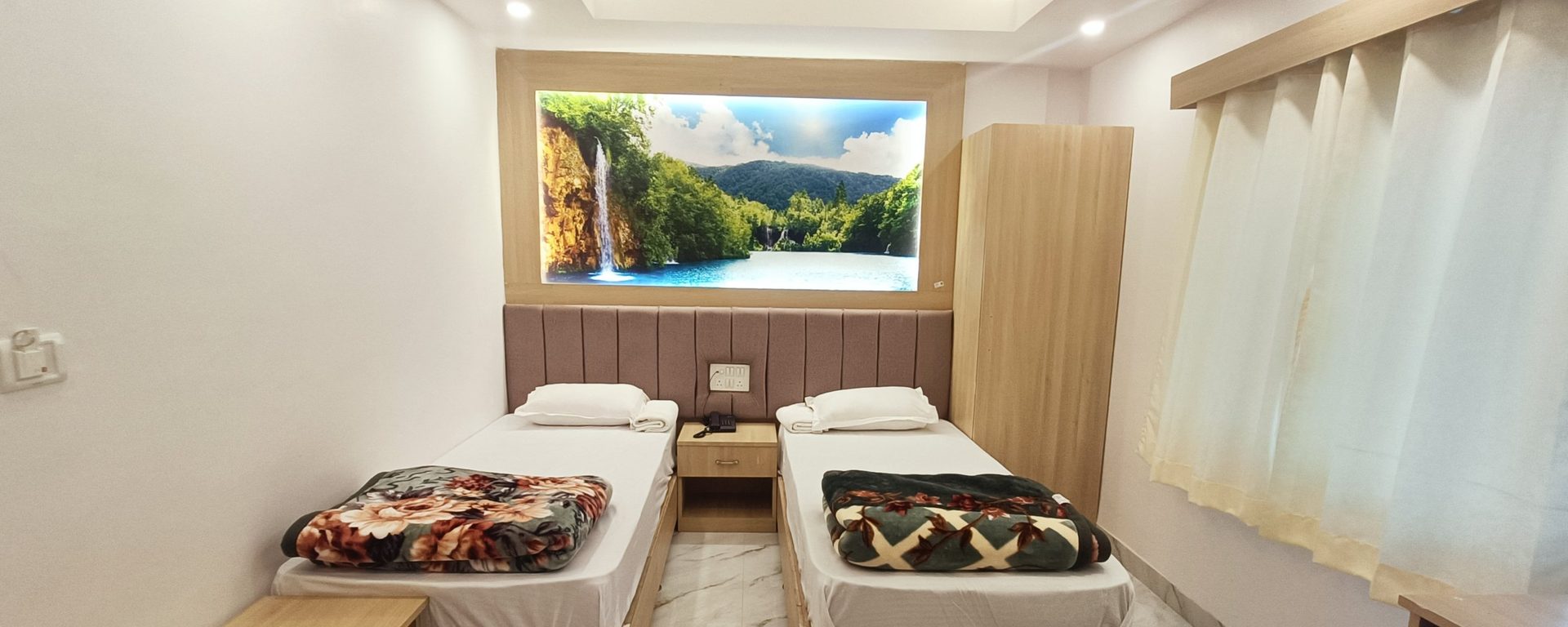 Deluxe room with two single beds beneath a backlit waterfall-and-lake panel